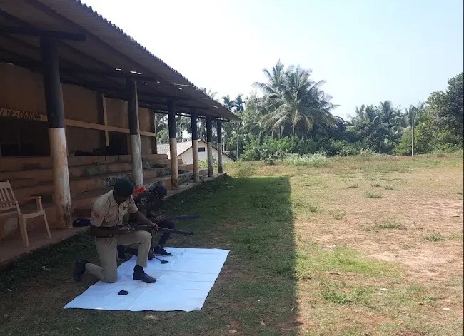 An NCC cadet and instructor beside rifles laid out for training
